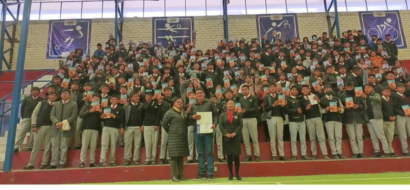 David Vildoso con cientos de estudiantes sosteniendo sus libros en un estadio escolar
